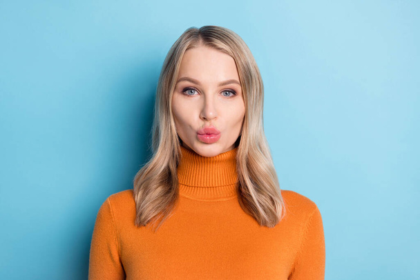 Photo of sweet flirty young woman dressed orange pullover sending you kiss isolated blue color background - 写真・画像