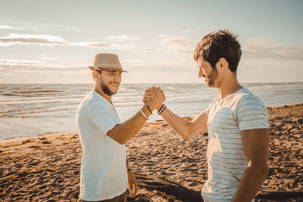 Портрет двох усміхнених хлопців на пляжі тремтять руки - Щасливі найкращі друзі вітають один одного рукостисканням
 - Фото, зображення