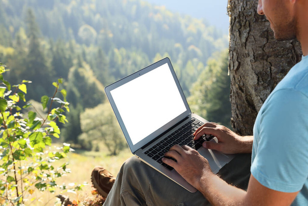 Man working on laptop outdoors surrounded by beautiful nature, closeup. Space for text - Фото, зображення