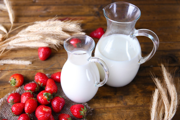 Ripe sweet strawberries and jug with milk on color wooden background - Фото, изображение