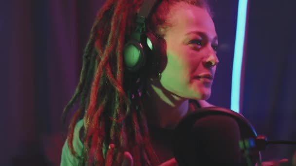 close-up shot van gelukkige jonge vrouw met dreadlocks vertellen haar verhaal op podcast in studio met neon string lichten - Video