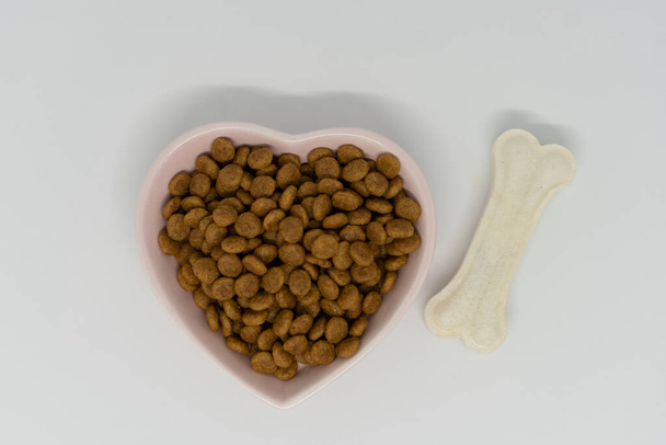 Dog food in a heart-shaped bowl, next to a white dog bone - Фото, изображение