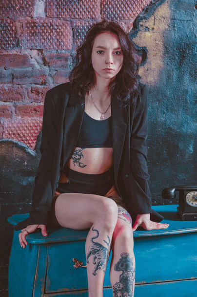 girl with tattoos sits on a dresser in a jacket and underwear - 写真・画像
