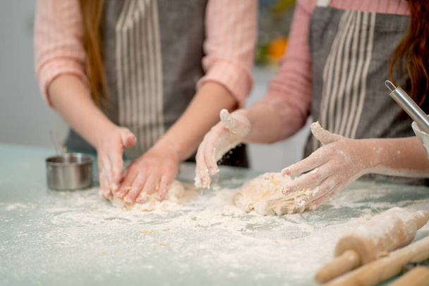 休日やリラックスした時間の間に一緒に家族の活動のように見えるキッチンで他のツールやアクセサリーで調理するための2人の女性の手を閉じて小麦粉. - 写真・画像