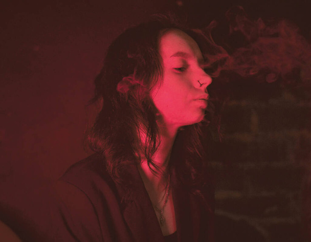 ジャケットにタトゥーのある女の子とセクシーな喫煙赤いネオンでタバコ - 写真・画像