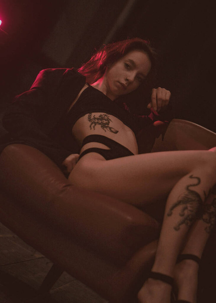 girl with tattoos in a jacket and sexy shoes in red neon - Foto, Imagem