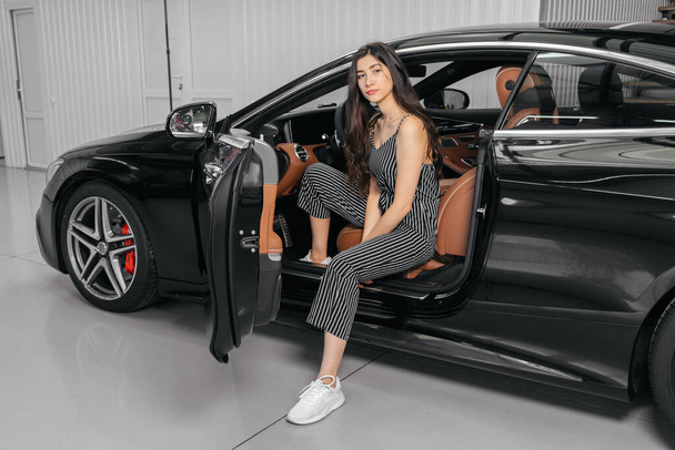 Jovem mulher asiática sentada em carro de luxo na garagem antes de iniciar o motor - Foto, Imagem