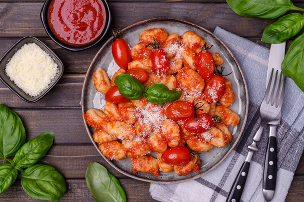 Gnocchi with tomatoes, red sauce, cheese and basil leaves on a brown wooden background. Top view. Selective focus. - Фото, зображення