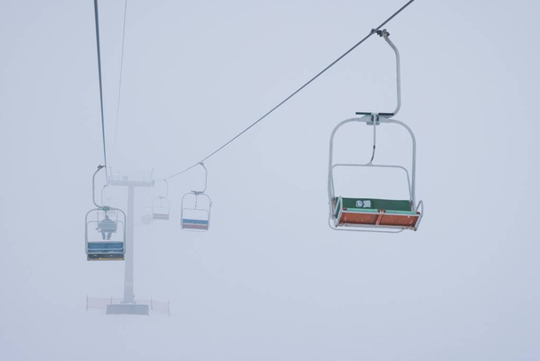 Cable cars hang on cables in a silent ski resort against a foggy sky - Foto, afbeelding