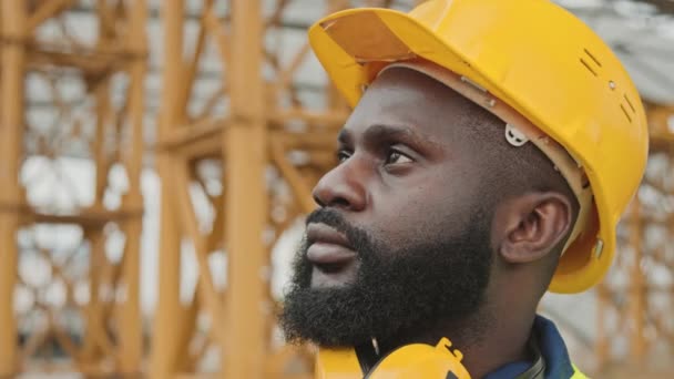 Primer plano de un trabajador afroamericano con sombrero duro que se pone gafas de seguridad en el sitio de construcción - Metraje, vídeo