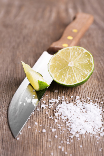Still life with fresh lime, knife and salt on old wooden table - Фото, зображення