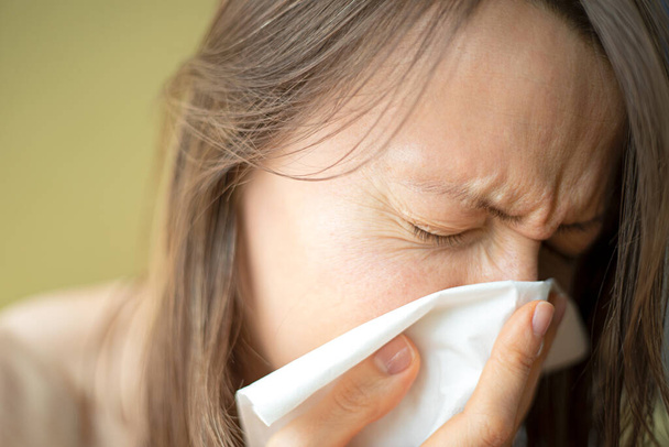 Przeziębienie lub objawy grypy wieńcowej. Młoda kobieta z alergią kichająca w chusteczkę, by zapobiec rozprzestrzenianiu się choroby o immunitet. - Zdjęcie, obraz