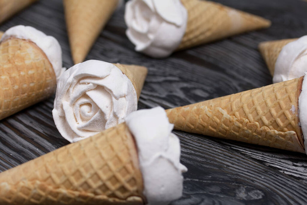 Homemade marshmallows are spread out on the table surface. Zephyr in a waffle cone. Made in the shape of a rose. Close-up shot. - Fotografie, Obrázek