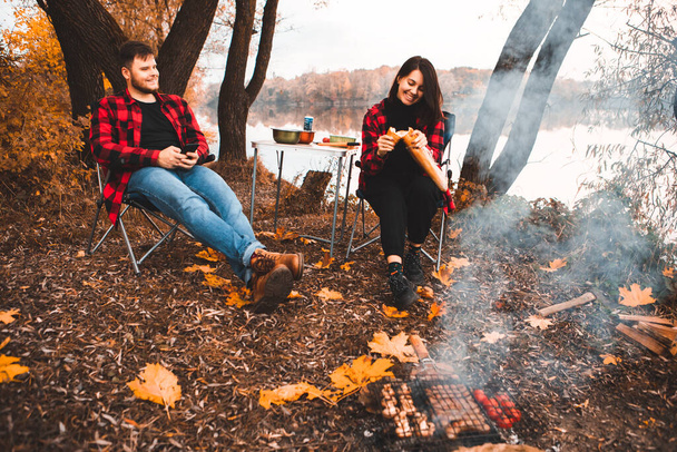 smiling happy couple resting near fire cooking food autumn camping concept - Photo, Image