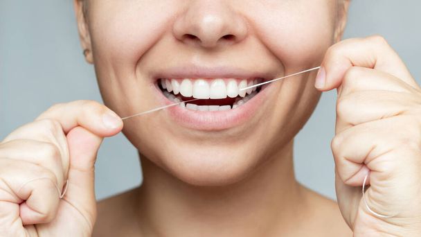 Cropped shot of a young beautiful caucasian woman flossing her teeth isolated on a gray background. Oral hygiene, dental health care, morning and evening routine.  - 写真・画像