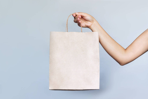 Paper eco friendly bag with copy empty space for the logo in a female hand isolated on a light gray background. Mockup, template for text or design. Shopping and fashion - Photo, image