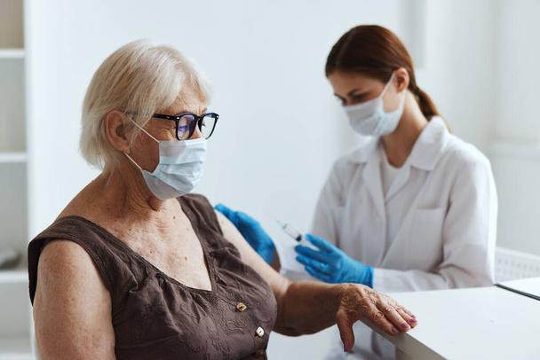 anziana donna con una maschera medica seduta accanto al passaporto del vaccino infermiere - Foto, immagini
