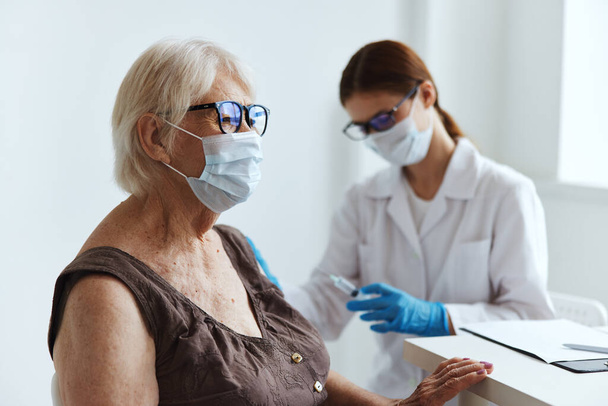 Yaşlı bir kadın sağlık hizmetinin tıbbi maske aşısı - Fotoğraf, Görsel