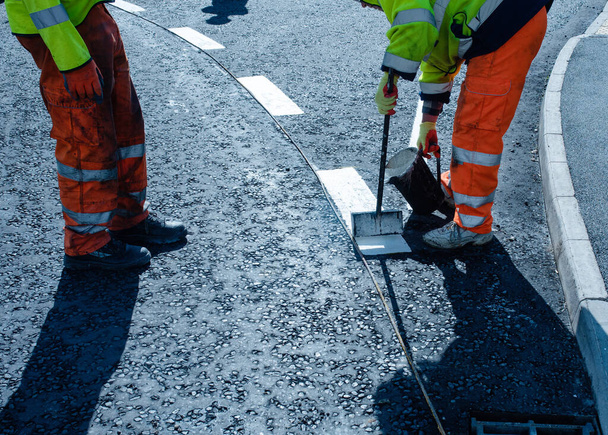 Straßenarbeiter bringen während des neuen Kreisverkehrs und der Erschließungsstraße thermoplastische Fahrbahnmarkierungen auf dem frisch verlegten Asphalt an - Foto, Bild