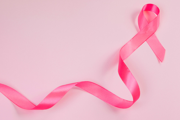 Pink ribbon on colored background. Breast Cancer Awareness Month symbol. Women's health care concept. Promotion of campaign to fight cancer. Copy space. - Photo, Image