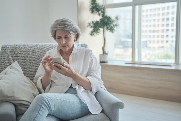 Thoughtful serious mature old 60s woman woman using smartphone worried about chatting with children - Photo, Image