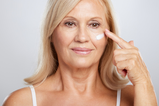 An attractive blond senior woman putting anti-age creme. Beauty photography - Photo, Image
