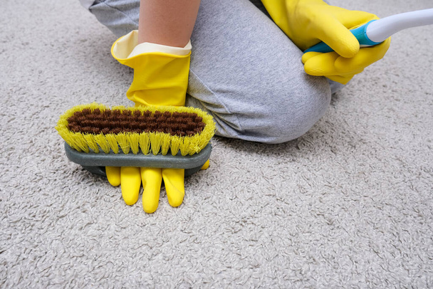 A child in yellow rubber gloves cleaning house, carpet from dust and stains with a brush - Photo, image