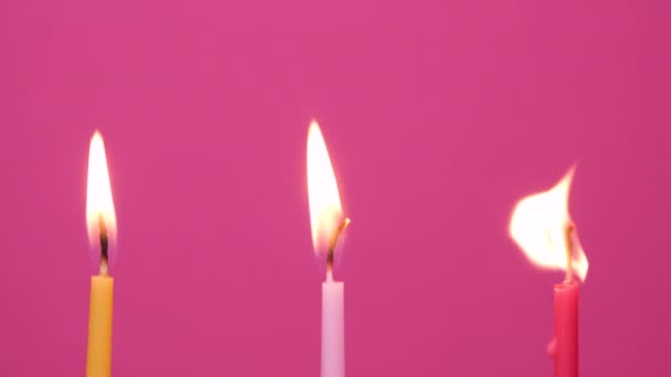 Soffiando tre candele di torta che bruciano su uno sfondo rosa. Avvicinati alle candele gialle, rosa e magenta. 4K risoluzione video - Filmati, video
