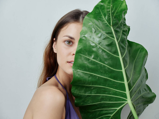 pretty woman covers half of her face with green leaf swimsuit cropped view - Photo, Image