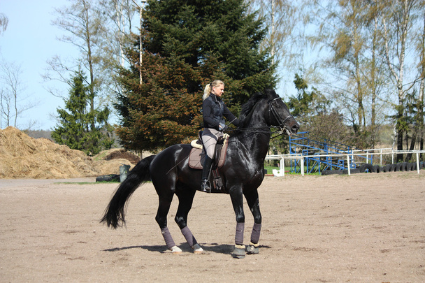 Mujer rubia montando caballo negro
 - Foto, Imagen
