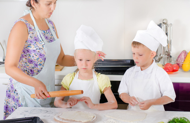 Äiti opettaa kaksi lasta leipoa
 - Valokuva, kuva