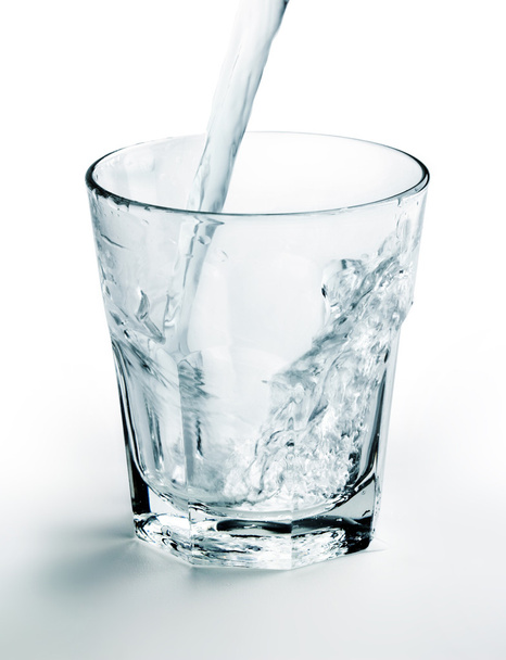 waterstraal vullen een glas op witte achtergrond - Foto, afbeelding