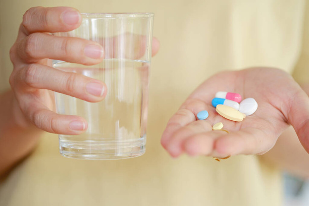 Φάρμακα και νερό στο χέρι μιας γυναίκας επειδή τρώει για τη θεραπεία της ασθένειας. Έννοια υγειονομικής περίθαλψης. - Φωτογραφία, εικόνα