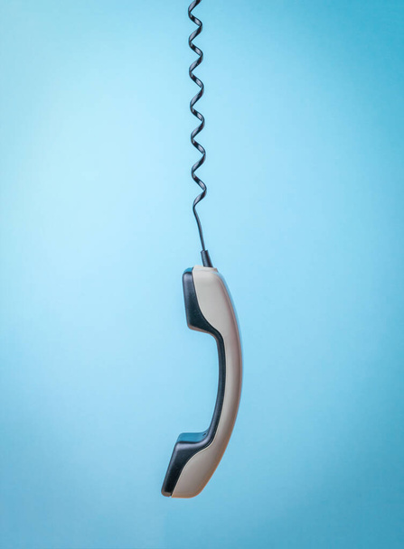 A gray handset on a stretched telephone wire on a blue background. Retro communication equipment. - Фото, зображення