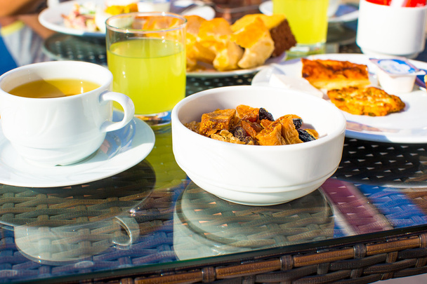 Delicioso desayuno con copos, fruta seca y taza de té
 - Foto, Imagen