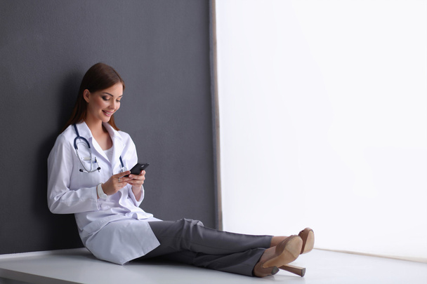 Young woman doctor sitting on the floor with your phone - Valokuva, kuva