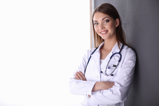 Doctor woman with stethoscope standing near grey wall - Фото, изображение