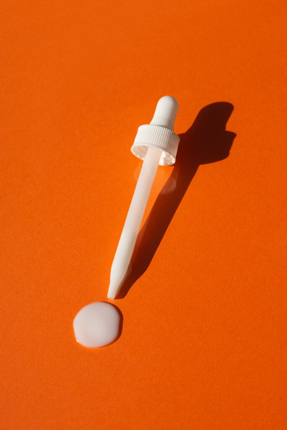 Open cap with dropper pipette with serum. Orange background with the appearance of the texture of the cream. - Photo, Image