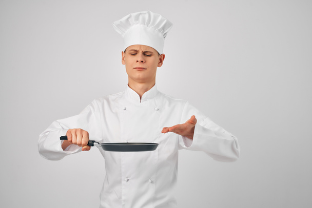 een man in een koks uniform een koekenpan in de hand koken voedsel in de keuken - Foto, afbeelding