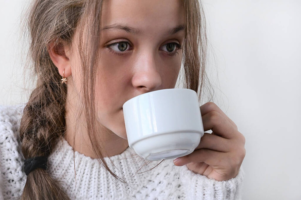 pretty girl in knitted warm sweater drinks from white cup, warms up. Concept of winter rest and comfort. Close-up. Copy space - Φωτογραφία, εικόνα