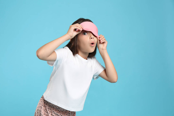 Cute girl wearing pajamas and sleeping mask on light blue background - 写真・画像