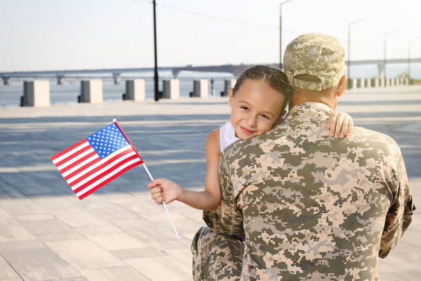 Soldier and his little daughter with flag of USA hugging outdoors - Fotoğraf, Görsel