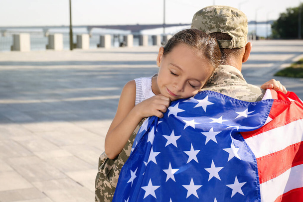 Soldier with flag of USA and his little daughter hugging outdoors, space for text - Foto, Imagen
