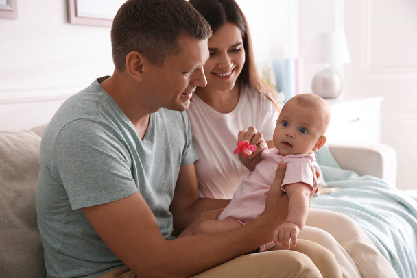 Happy couple holding their cute little baby with pacifier at home - Foto, Imagen
