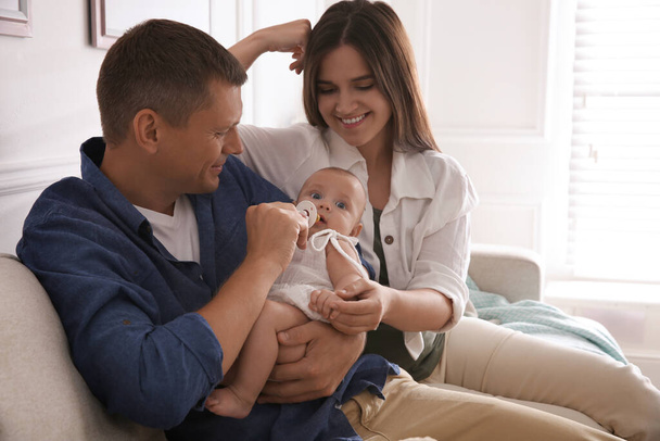 Happy couple holding their cute little baby with pacifier at home - Photo, Image