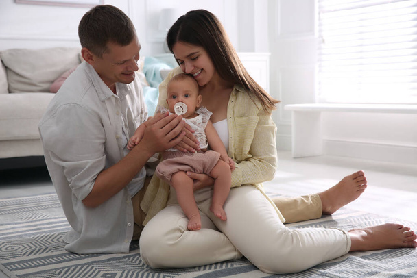 Happy couple holding their cute little baby with pacifier at home - Photo, image
