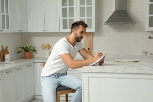 Handsome man with notebook sitting on stool in kitchen - Fotografie, Obrázek