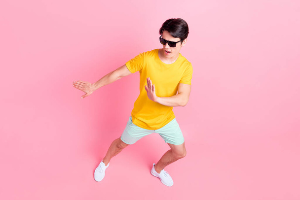 Foto von süßen funky jungen Kerl gekleidet gelbes T-Shirt dunkle Brille tanzen lächelnd isoliert rosa Farbe Hintergrund - Foto, Bild