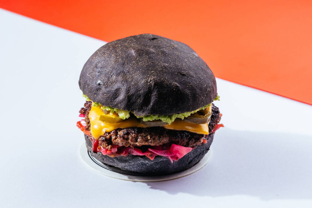 Siyah çörekler ızgara et burger, peynirli ve domatesli kırmızı arka plan.  - Fotoğraf, Görsel