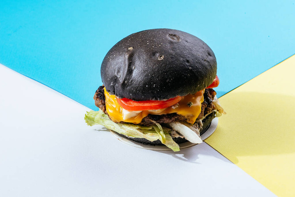 hamburguesa de carne de bollos negros con queso y tomates sobre fondo azul  - Foto, imagen